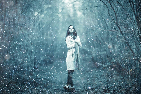 Portrait of young beautiful woman in park with snowflakes in the air