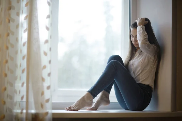 Triste adolescente sentada no peitoril da janela — Fotografia de Stock