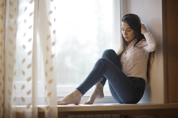 Teenage girl sitting on windowsill — Stock Photo, Image