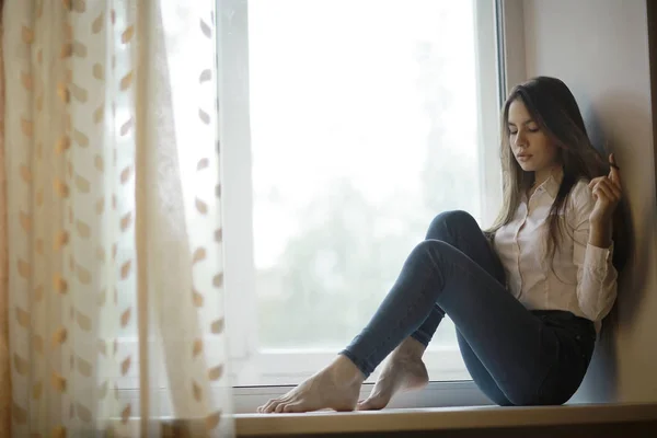 Triste adolescente sentada no peitoril da janela — Fotografia de Stock