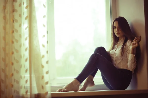 Sad teenage girl sitting on windowsill — Stock Photo, Image