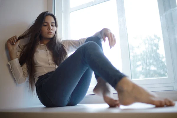 Teenage girl sitting on windowsill — Stock Photo, Image