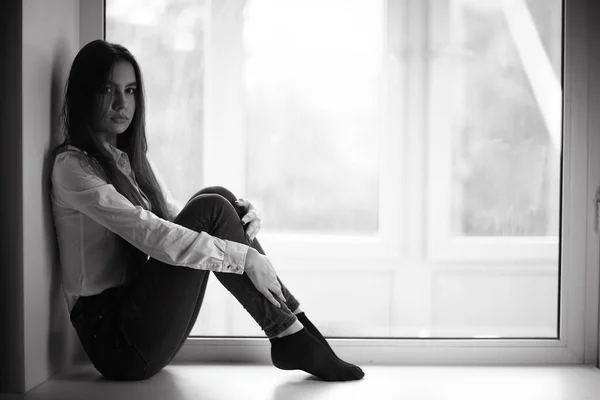 Sad teenage girl sitting on windowsill — Stock Photo, Image