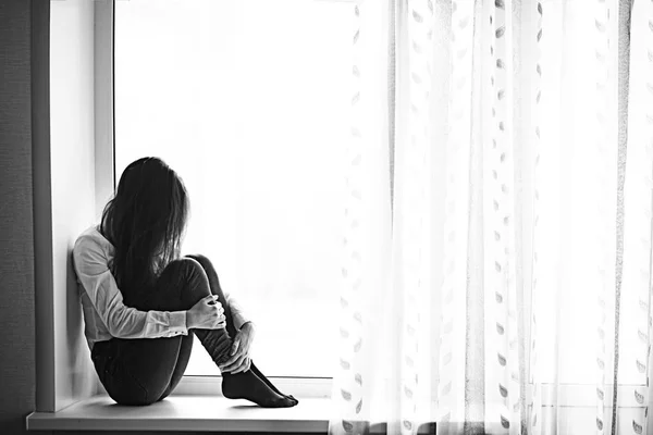 Sad teenage girl sitting on windowsill — Stock Photo, Image