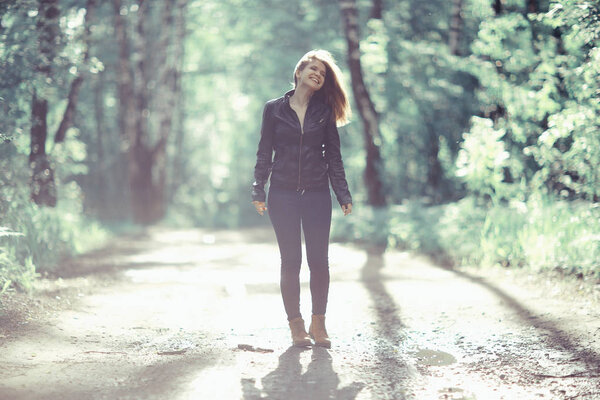 Young beautiful happy woman in leather jacket walking in park