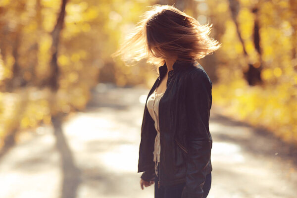 Young beautiful happy woman in leather jacket walking in park