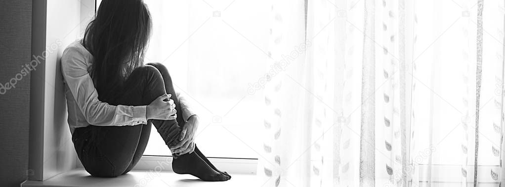 sad teenage girl sitting on windowsill