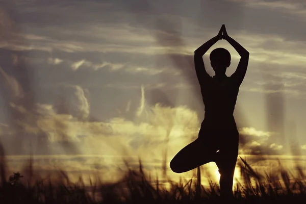 Жінка робить йогу проти заходу сонця неба — стокове фото