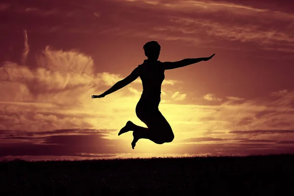 Mujer saltando contra el cielo puesta del sol — Foto de Stock