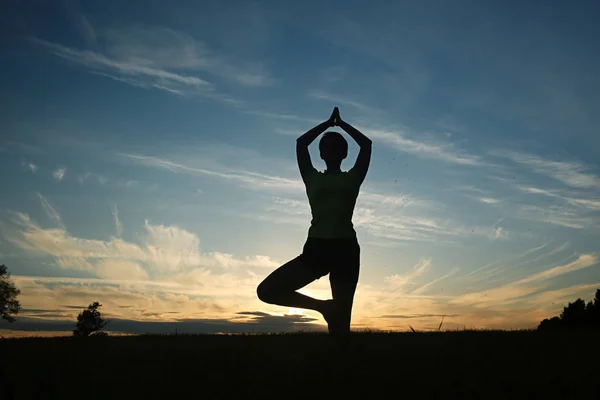 Жінка робить йогу проти заходу сонця неба — стокове фото