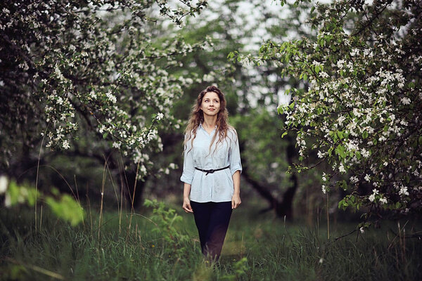 Young happy woman enjoying bloom of apple trees in spring garden