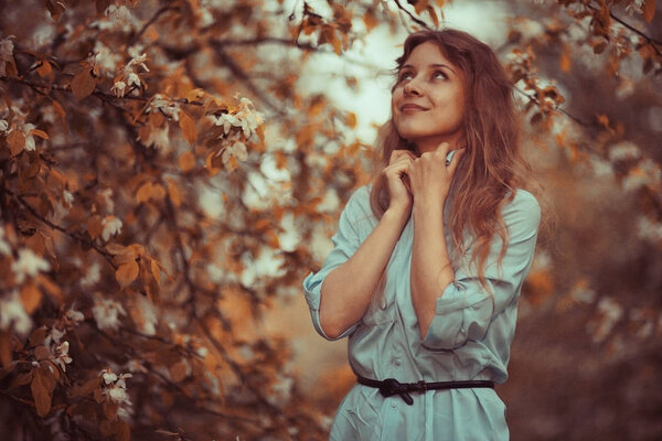 Young happy woman enjoying bloom of apple trees in spring garden, yellow leaves effect