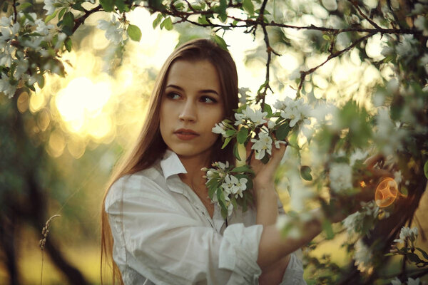 Portrait of young beautiful woman with apple blossom in spring garden