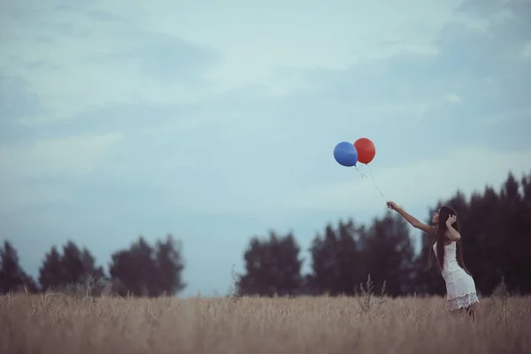 Nainen vehnäpellolla lentävien ilmapallojen kanssa — kuvapankkivalokuva