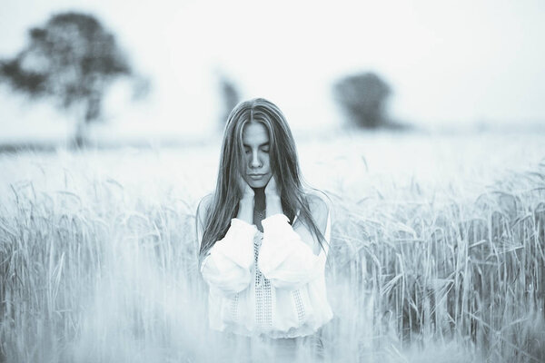 Dreaming beautiful young woman with long hair in wheaten field