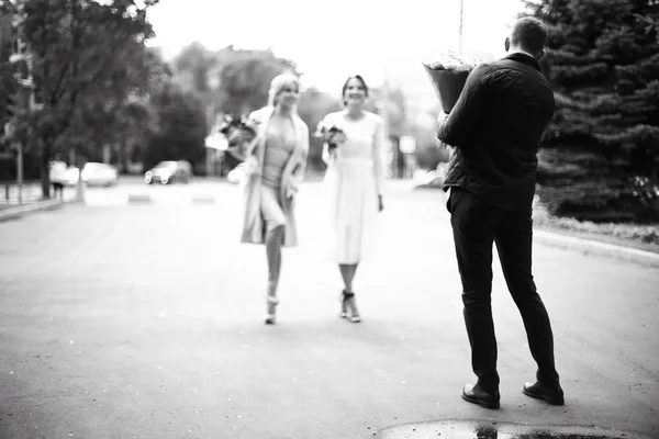 Cheerful guests at wedding, back view of man in suit holding bouquet of flowers, black and white