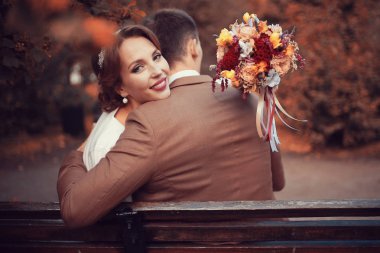 güzel genç gelin buketi çiçek ve yakışıklı Damat Düğün gününde parkta bankta oturmuş ile