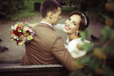 güzel genç gelin buketi çiçek ve yakışıklı Damat Düğün gününde parkta bankta oturmuş ile