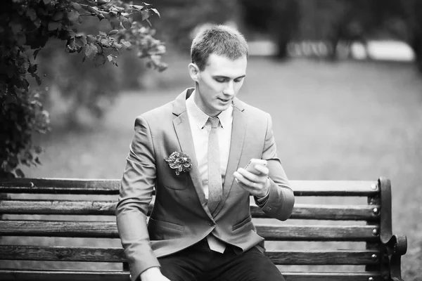 yakışıklı genç damat park bankta oturan ve smartphone kullanarak takım 