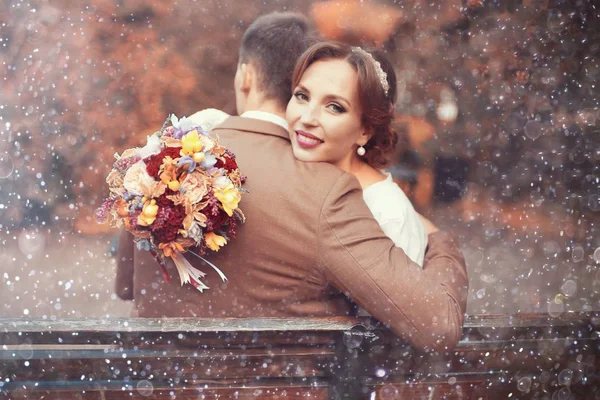 花とハンサムな新郎の結婚式の日に公園のベンチに座っての花束と美しい若い花嫁 — ストック写真