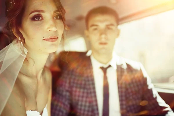 美丽的年轻新娘和快乐英俊的新郎坐在一起的车 — 图库照片