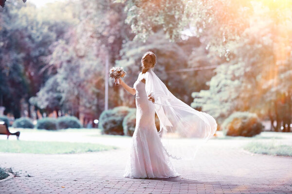 Beautiful bride in white wedding dress posing in summer park