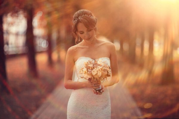 Beautiful bride in white wedding dress with bouquet of flowers posing in summer park