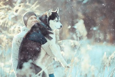 young man hugs a husky dog in the winter in the forest, a man and a dog hug together and play in a winter nature landscape