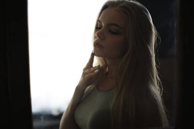 Genç, sarışın, uzun saçlı, şık bir model stüdyoda poz veriyor.