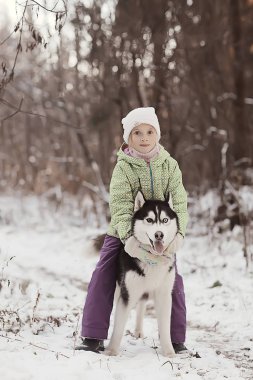 Çocuklar, güneşli bir ormanın kış manzarasında köpekle oynarlar. Kar yağışı yapan kızlar ve iri yapılı kızlar.