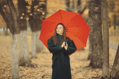 Şemsiyeli kız sonbahar parkında poz veriyor, Ekim manzaralı yalnız kadın elinde kırmızı bir şemsiye tutuyor.