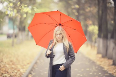 Sonbahar, güneşli bir gün. Şemsiyeli genç bir kız ekim ayında sarı bir parkta yürüyor.