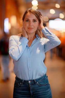 Beyaz kazaklı bir kız giyim mağazasında poz veriyor, uzun kollu pamuk kazak giyiyor.