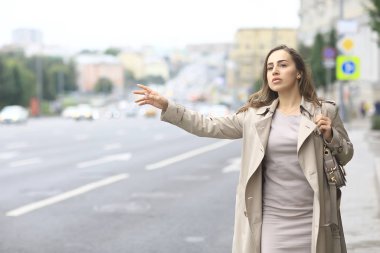 Kadın yolda bir araba yakalıyor, yetişkin genç bir kız taksi bekliyor, geçen bir aracı durduruyor, otostop çekiyor.