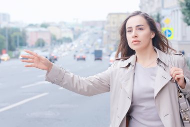 Kadın yolda bir araba yakalıyor, yetişkin genç bir kız taksi bekliyor, geçen bir aracı durduruyor, otostop çekiyor.