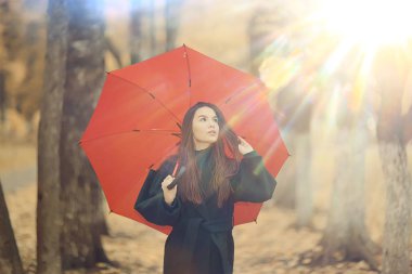 Sonbahar, güneşli bir gün. Şemsiyeli genç bir kız ekim ayında sarı bir parkta yürüyor.