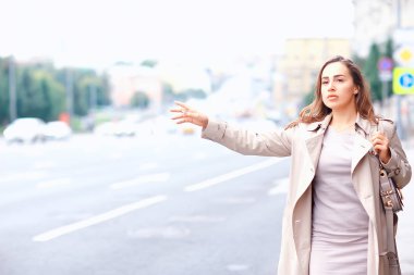 Kadın yolda bir araba yakalıyor, yetişkin genç bir kız taksi bekliyor, geçen bir aracı durduruyor, otostop çekiyor.
