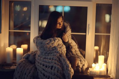 Pencerenin önünde battaniyede oturan kız, mumlar gece, yalnızlık, genç yalnız kız, stres