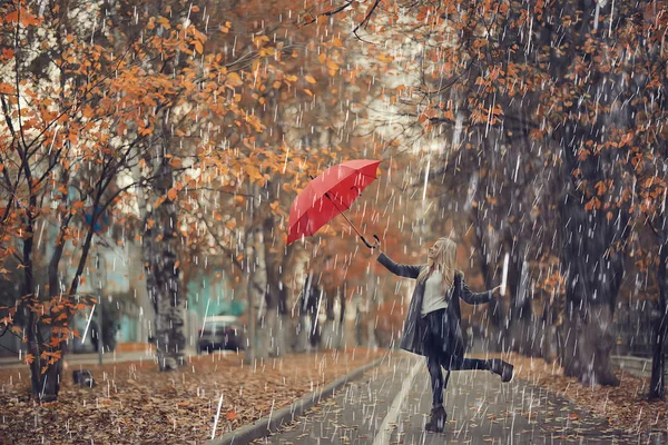 October walk in the rain, a young woman with a red umbrella in the autumn city park, autumn look