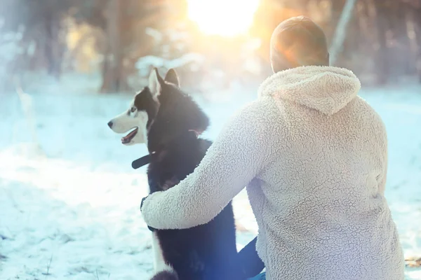 若い男が森の中で冬に犬を抱きかかえ男と犬は一緒に抱擁し冬の自然景観で遊ぶ — ストック写真