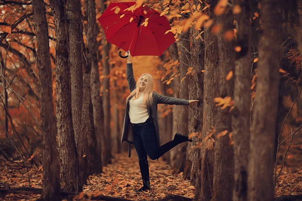 一个拿着红色雨伞的女孩 坐在雨伞上 跳跃着 在黄色的秋天的风景中享受着乐趣 — 图库照片