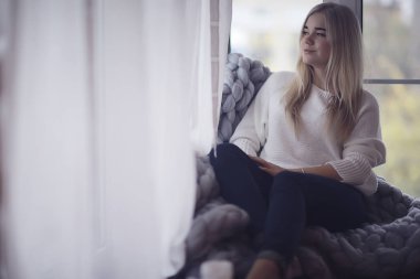 Ev cana yakın kız ekose pencere, ev sonbaharı görünümü, sıcak örgü örülmüş battaniyenin içindeki model ısınıyor.