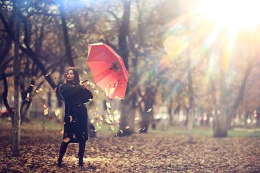 Sonbahar, güneşli bir gün. Şemsiyeli genç bir kız ekim ayında sarı bir parkta yürüyor.