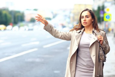 Kadın yolda bir araba yakalıyor, yetişkin genç bir kız taksi bekliyor, geçen bir aracı durduruyor, otostop çekiyor.