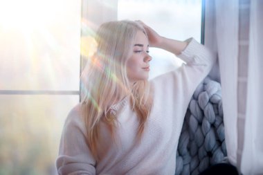 Kışın evin içinde, örnek bir kız pencerede örgü örüp güneşleniyor, evde soğuk bir gün.