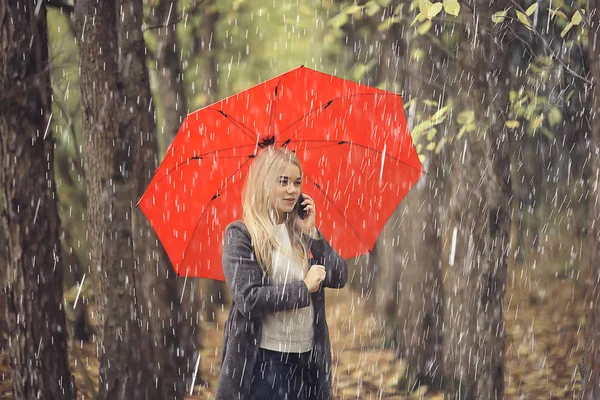 October walk in the rain, a young woman with a red umbrella in the autumn city park, autumn look