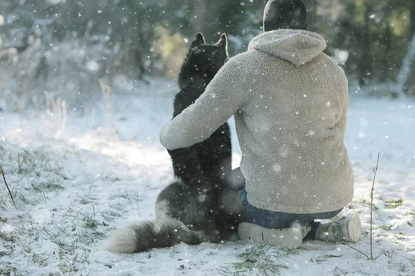 若い男が森の中で冬に犬を抱きかかえ男と犬は一緒に抱擁し冬の自然景観で遊ぶ — ストック写真