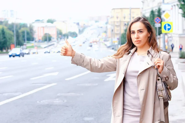 Kadın yolda bir araba yakalıyor, yetişkin genç bir kız taksi bekliyor, geçen bir aracı durduruyor, otostop çekiyor.