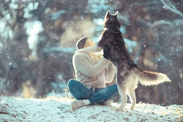 若い男が森の中で冬に犬を抱きかかえ男と犬は一緒に抱擁し冬の自然景観で遊ぶ — ストック写真