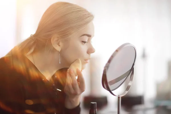 makeup girl at home by the mirror, young blonde adult model, face cosmetics concept